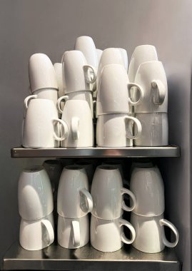 Ticari bir mutfakta ya da kafede paslanmaz çelik bir rafta baş aşağı duran temiz beyaz seramik kahve fincanları. Tekrarlama, temizlik ve işlevselliğe odaklı minimalist kompozisyon.