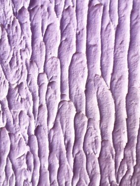 Yumuşak lavanta rengine boyanmış soyut alçı duvar dokusunun yakın çekimi. Yüzeyde sanatsal boya ya da alçı desenlerine benzeyen kalın, dikey rahatlama vuruşları var..