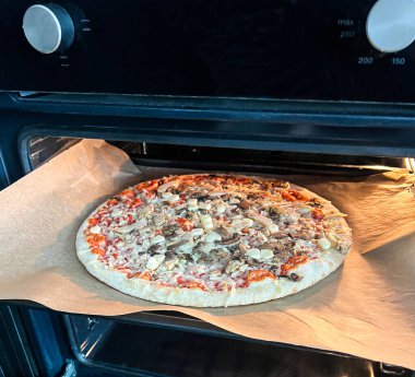 Çiğ donmuş pizza, peynirli, mantarlı, mısırlı ve salamlı fırının içine konmuş. Ev yapımı yemek ve fast food hazırlama konsepti.
