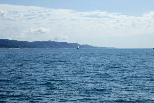 Karadeniz 'in mavi gök mavisi suyu ve ışık dalgalarıyla manzarası, merkezinde beyaz yelkenli bir yat ve ufukta tepeler. Yüksek kalite fotoğraf