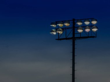 Alacakaranlıkta bir futbol stadyumunda aydınlık stadyum ışıkları. Yapının arkasında derin mavi bir gökyüzüne karşı bir podyum var..
