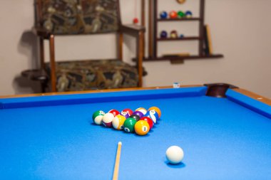 The photo shows a billiard table with a neat arrangement of billiard balls resting on the blue felt surface. The vibrant colors of the balls red, yellow, blue, green, and black stand out against the smooth, rich blue backdrop. 