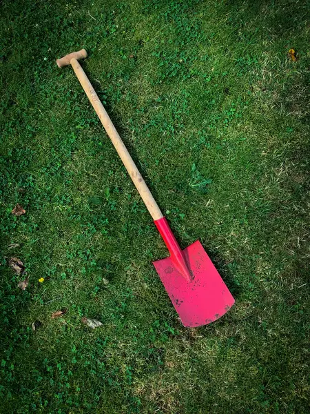 Yeşil bir çayırda büyük kırmızı bir kürek.