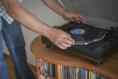 Almanya. 24 Ağustos 2024. İnsan eli oturma odasında retro vinil plak çalar üzerine plak koyar.