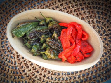 Kızarmış Pimientos de Padron ve kırsal seramik bir tabakta servis edilen kırmızı biberler. Zengin dokusuyla otantik bir Akdeniz mezesi.