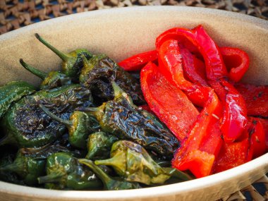 Kızarmış Pimientos de Padron ve kırsal seramik bir tabakta servis edilen kırmızı biberler. Zengin dokusuyla otantik bir Akdeniz mezesi.
