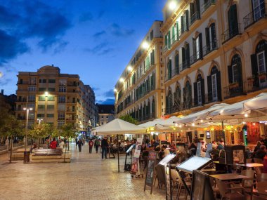 Malaga, İspanya. 7 Mart 2025. Gün batımında Mlaga 'daki Plaza de la Merced' in atmosferik manzarası ılık aydınlatma, hareketli kafeler ve zengin İspanyol kültürü. (Tanınabilir kişiler ve marka isimleri dijital olarak kaldırıldı)