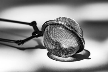 Çay süzgeci maşalarının siyah ve beyaz fotoğrafı, minimalist tasarımı vurgulamak, pratik çay demleme kullanımı ve zarif mutfak aksesuarları.