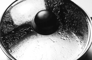 Buhar mutfağını temsil eden buhar damlacıklarıyla kaplı cam kap kapağını kapatın. Ev işleri ve temiz modern yemek hazırlama.