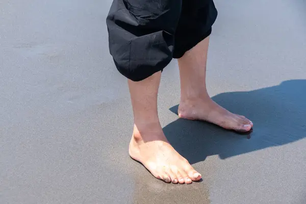 Siyah kumsalda oynayan bir kadının ayakları, eşsiz bir sahil şeridinde yalınayak özgürlük ve doğal güzelliğin huzurlu bir anını yakalıyor.