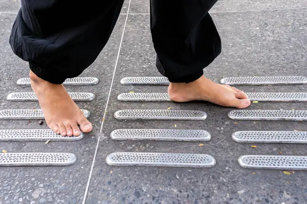 Bir kişi, görme engelli yayalara yardım etmek için özel olarak tasarlanmış kılavuz bloklarla donatılmış bir kaldırım boyunca yürür. Kılavuz bloğunun yükseltilmiş dokunsal yüzeyi, kamu alanlarını güvenli bir şekilde dolaşmak için kritik bilgiler sunar.