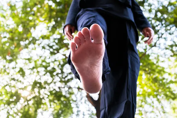 Bir kadının ayağının yakın çekimi, yumuşak, bulanık yeşil yaprakların arka planıyla tezat oluşturur. Görüntü, basitlik ve doğal güzelliği vurgulayarak, insan ve doğa arasındaki huzurlu bağlantıyı yakalar.