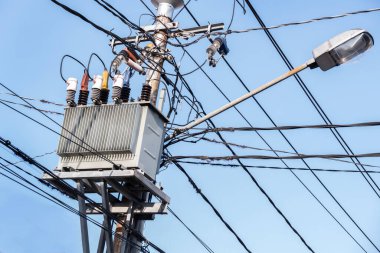 Şehir direğinin tepesinde karmaşık kablolar bulunan bir trafo, enerji sistemlerinin korunmasında güç altyapısının kritik rolünün altını çiziyor.