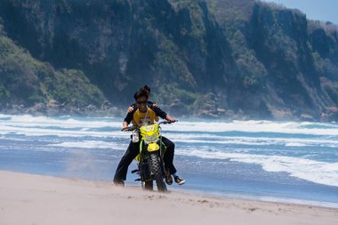 Yogyakarta, Endonezya - 11 Eylül 2024: İki genç çocuk Parangtritis Sahili 'nde motokros sürerek macera sporlarının tadını çıkarıyor. Heyecan arayan motokros hayranları için kumda mükemmel bir off-road bisikleti eğlencesi.
