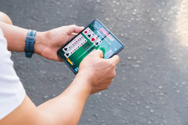 Yogyakarta, Endonezya - 11 Eylül 2024: Mobil kart oyunlarına kendini kaptırmış bir adam akıllı telefon oyunlarının büyük oyun endüstrisini nasıl etkilediğini vurguluyor