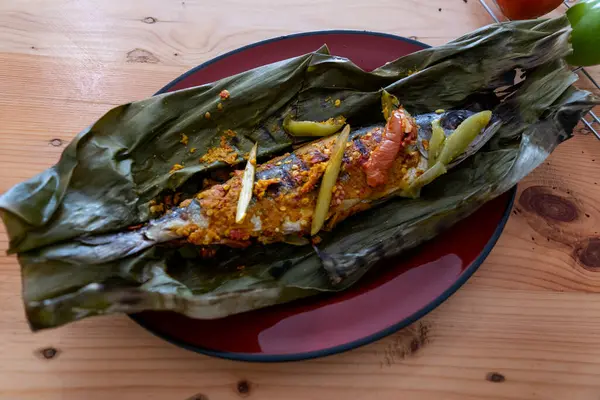 Pepes Ikan. Ahşap masada muz yapraklarına sarılı geleneksel Endonezya buğulama balığı. Yüksek Açı Görünümü