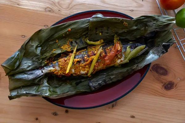 Pepes Ikan. Ahşap masada muz yapraklarına sarılı geleneksel Endonezya buğulama balığı. Üst Görünüm