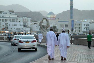 Bir çift yerli Ummani adam akşam saatlerinde Muscat, Umman 'da Muttrah Corniche boyunca yürür.