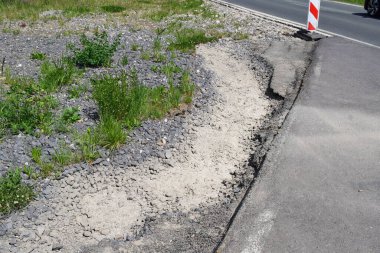 Yol, derin bir çukur ve yeşil çimlerde beyaz kumla kaplı.