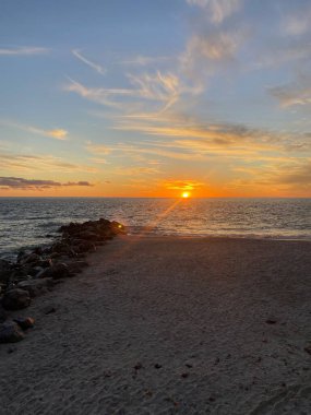 Güneş okyanusun üzerinde batıyor, kumlu kıyılara sıcak bir parıltı saçıyor..