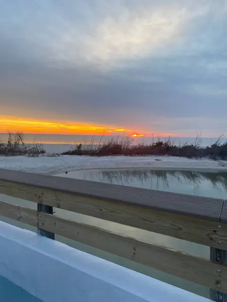 Gün batımında, bulutlu bir gökyüzü ve sakin bir suyla sahile bakan bir sahil yolu..