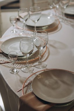 Zarif tabaklar, şık şarap bardakları ve davetkar bir yemek deneyimi için güzelce katlanmış peçetelerle güzel bir şekilde hazırlanmış bir masa.