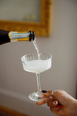 A woman is carefully pouring champagne into a glass, creating a fine effervescence as the bubbles rise and dance within the vessel