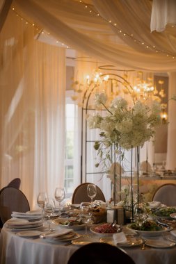 Zarif tabaklar, pırıl pırıl bardaklar ve renkli çiçeklerle süslenmiş bir düğün resepsiyonu için güzel bir masa seti.