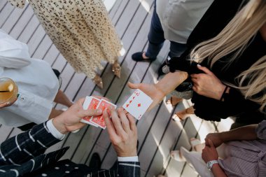 Canlı bir grup insan, ahşap bir güvertede heyecanlı bir iskambil oyunuyla meşgul. Kahkahalarını ve güzel zamanlarını paylaşıyorlar.