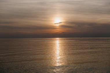 Güneş ufkun ötesine inerken ılık ışığı yumuşak okyanus suyunun yüzeyine güzel bir şekilde yansıyor.
