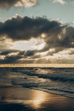 Güneş, aşağıdaki uçsuz bucaksız okyanusun üzerinde süzülen ince bulutların arasından çok güzel bir şekilde parlıyor. Göz kamaştırıcı bir görüntü yaratıyor.