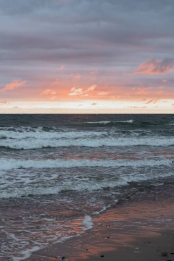 Dalgaların sürekli kumlu sahile çarptığı ve huzurlu bir atmosfer yarattığı engin okyanus üzerinde nefes kesici bir gün batımı.