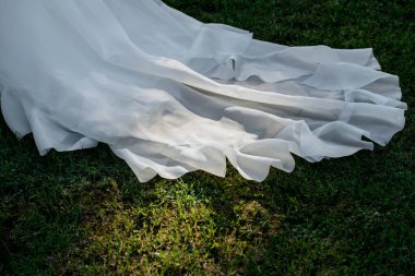 Akan beyaz bir gelinlik içindeki bir kadın, açık gökyüzünün altındaki yumuşak yeşil çimlerin üzerinde zarif bir şekilde yatıyor.