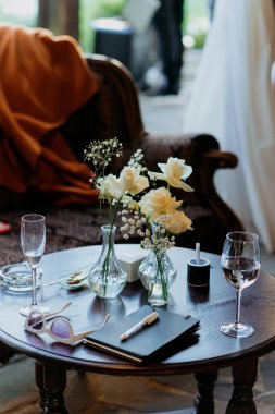 Zarifçe sergilenmiş zarif şarap kadehleriyle eşleştirilmiş, canlı çiçeklerle dolu dekoratif bir vazonun olduğu güzel bir masa.