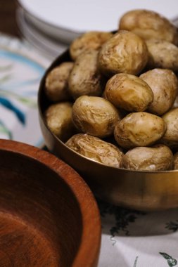 Hasat edilmiş patateslerle dolu bir kase ahşap bir masada, sahneyi tamamlamak için zarif bir şekilde hazırlanmış ahşap bir kasenin yanında duruyor.