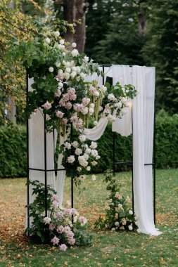 Zarif beyaz çiçekler ve yemyeşil çiçeklerle süslenmiş güzel bir düğün kemeri özel bir gün için güzel bir parka kurulmuştur.