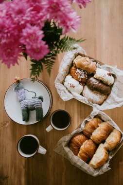 Büyüleyici ahşap bir masa, lezzetli çöreklerle dolu bir sepetle ve iki dumanı tüten kahveyle doludur.