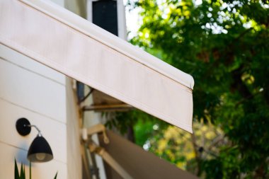 Modern bir binanın kenarından sarkan beyaz bir tente, cephesine gölge ve estetik cazibe sağlıyor.