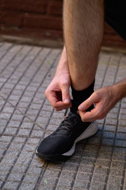 Bir adam ayakkabılarını pürüzsüz fayanslı zemine bağlamak için diz çöküyor. Güvenli bir şekilde bağlandıklarından emin olmaya odaklanıyor.
