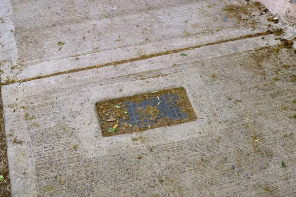 Kirli bir beton kaldırımda, üzerinde aşınmış bir paspas bulunur ve şehir ortamında doku ve renklerin kesişmesini sağlar.