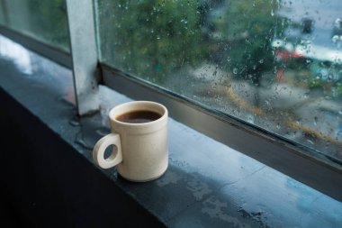 Dumanı tüten bir fincan kahve, pencerenin pervazında sakince duruyor, camdan süzülen güneş ışığının tadını çıkarıyor.