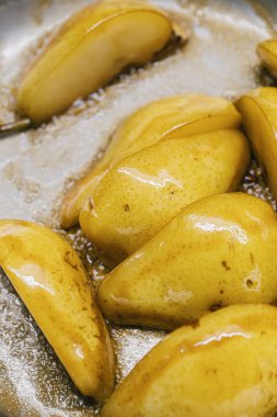 Lezzetli, sulu, karamelli armut dilimlerinin yakın plan görüntüsü. Parlak paslanmaz çelik bir tavada güzel pişiyor.