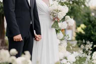 Güzel bir gelin ve yakışıklı bir damat, sevgi ve kutlamalarla çevrili neşeli düğün törenlerinde sıkıca el ele tutuşuyorlar.