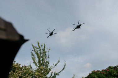 Ağaçların üzerinde, iki helikopter zarif bir şekilde gökyüzünün uçsuz bucaksız genişliğinde manevra yapıyor, havacılığın mucizelerini sergiliyor.