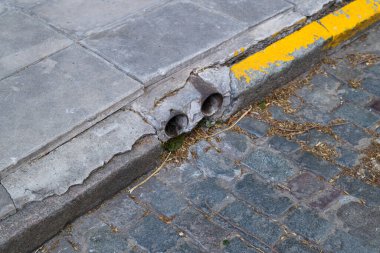 Tuğladan döşenmiş bir yolun kenarında, araçlar ve yayalar için net bir sınır çizimi sağlayan sarı bir kaldırım var.
