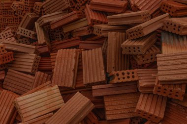 İnşaat alanında kırmızı ve kahverengi kil tuğlalardan oluşan bir dağ. Duvarcılıkta ve inşaatta kullanılan yapı malzemelerini gösteren dokunun yakın çekimi.