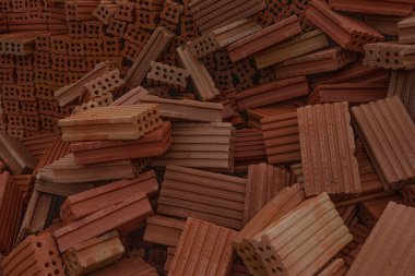 İnşaat alanında kırmızı ve kahverengi kil tuğlalardan oluşan bir dağ. Duvarcılıkta ve inşaatta kullanılan yapı malzemelerini gösteren dokunun yakın çekimi.