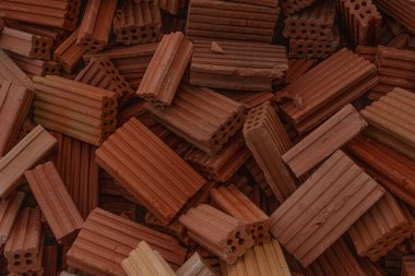 İnşaat alanında kırmızı ve kahverengi kil tuğlalardan oluşan bir dağ. Duvarcılıkta ve inşaatta kullanılan yapı malzemelerini gösteren dokunun yakın çekimi.