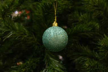 Dolgun yeşil iğnelerle çevrili bir Noel ağacının dalından sarkan parlak bir turkuaz Noel topu. Noel fotoğrafı