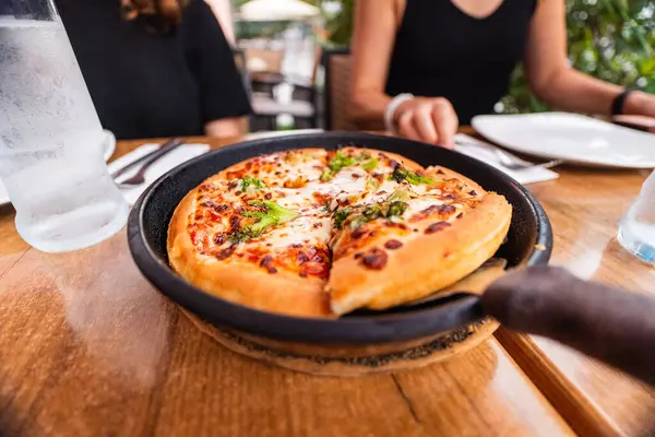 Peynirli bir tavada vejetaryen brokoli pizzası ve bir restoranda bir dilim pizza seçen fırınlanmış ekmek.